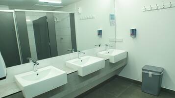 A modern bathroom with three sinks, a large mirror, and a trash bin.