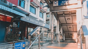 Een hotelentree met een trap naar de lobby, een bord met MRT Hua Lampone station en een bord voor kamers te huur.