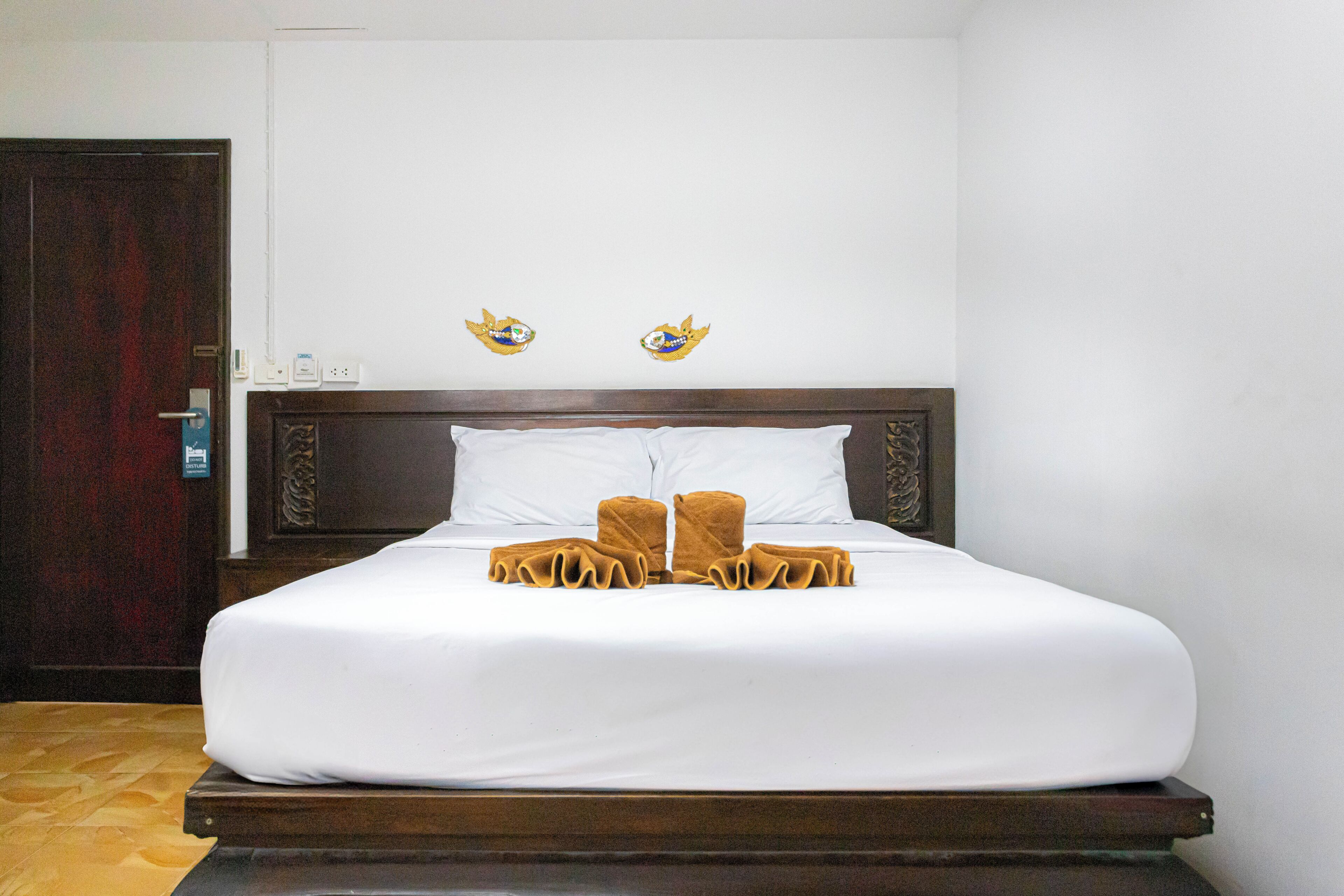 A neatly made bed with white sheets and two towels, a wooden headboard, and two wall-mounted wall art pieces.