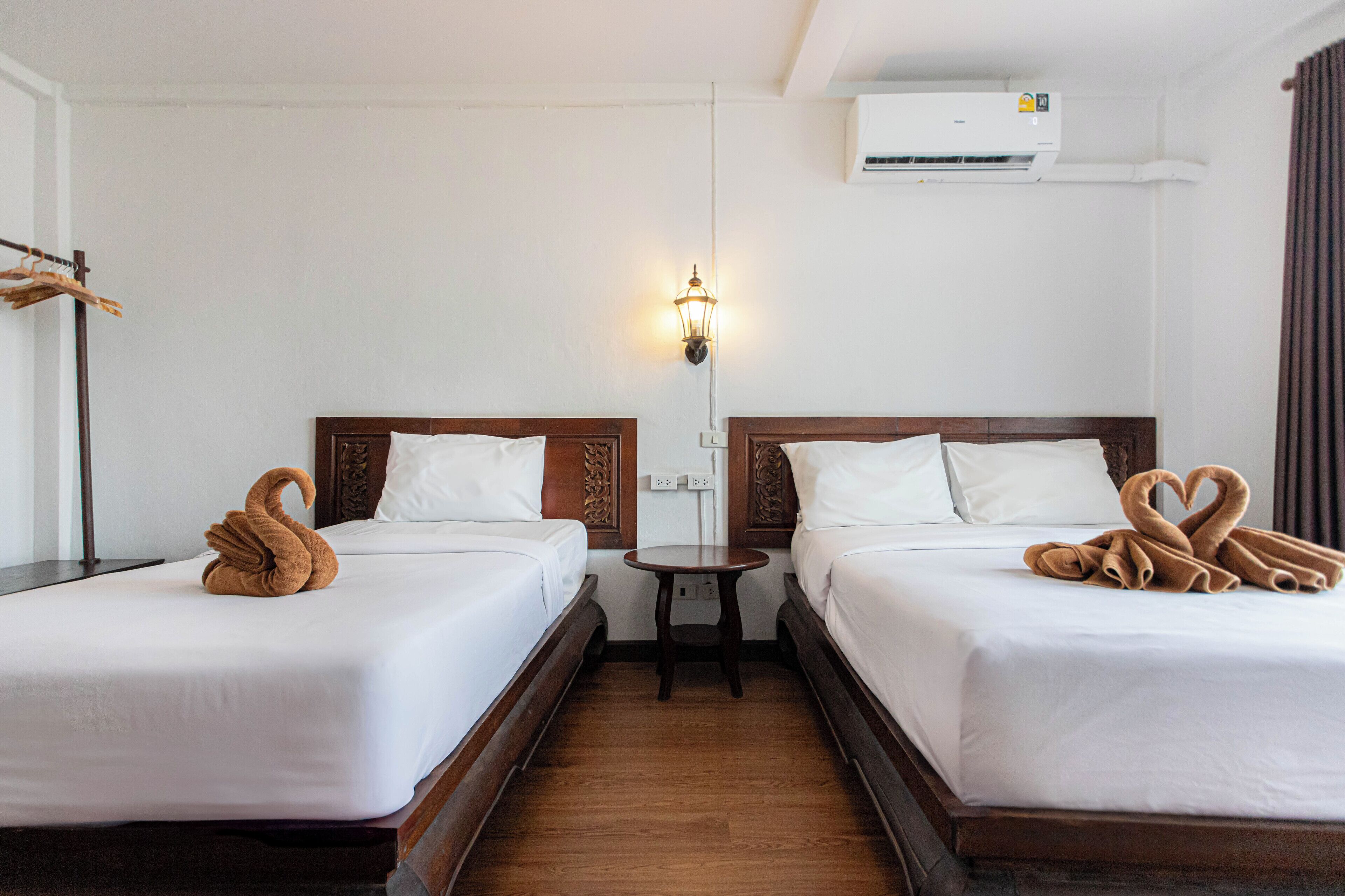 A hotel room with two beds, a bedside table, a wall-mounted air conditioner, and a wall-mounted light fixture.