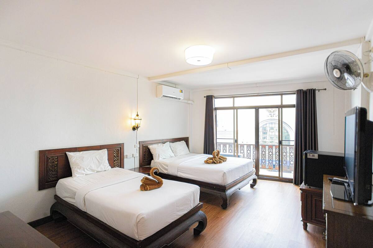 Habitación de hotel con dos camas, televisión, ventilador y balcón con vistas.
