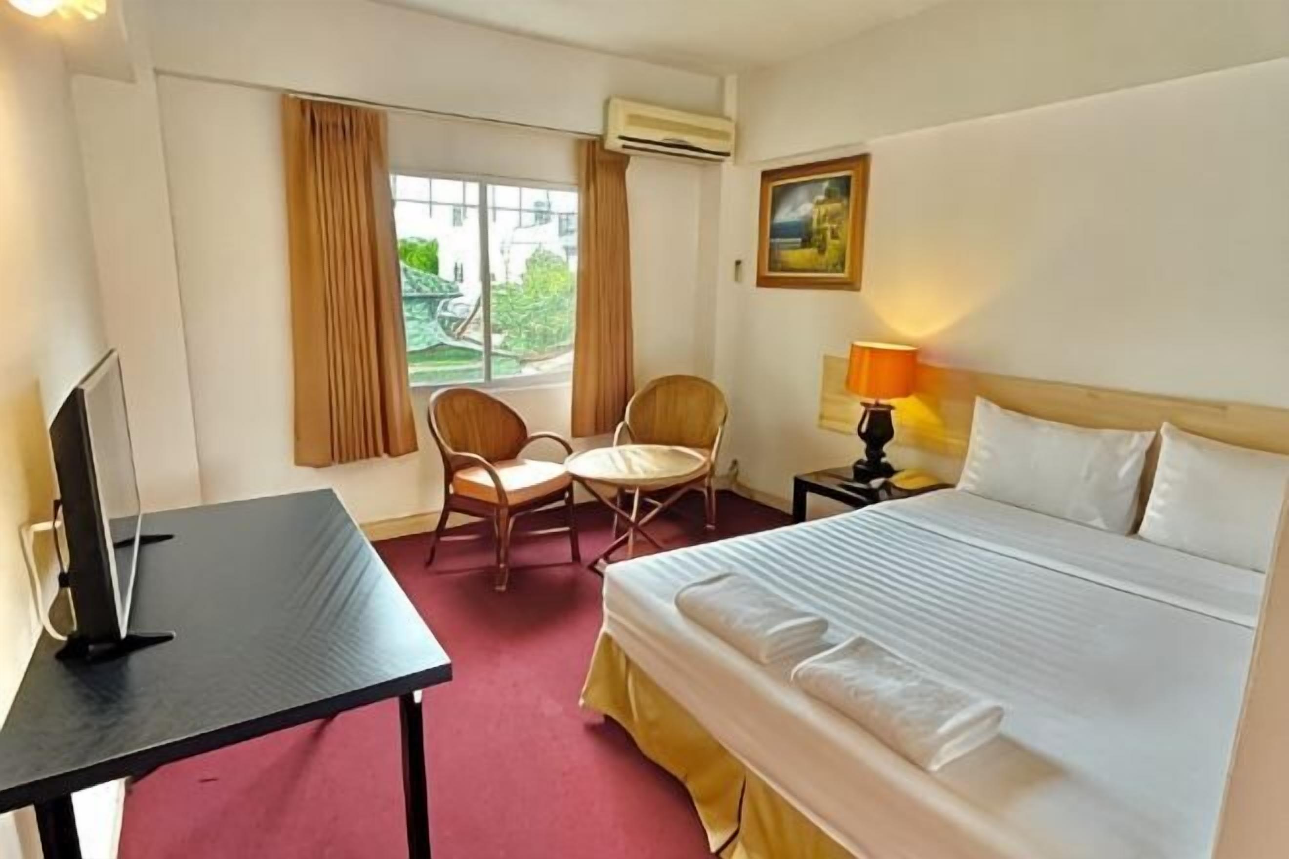 A hotel room with a bed, a desk, a chair, a lamp, and a window with curtains.