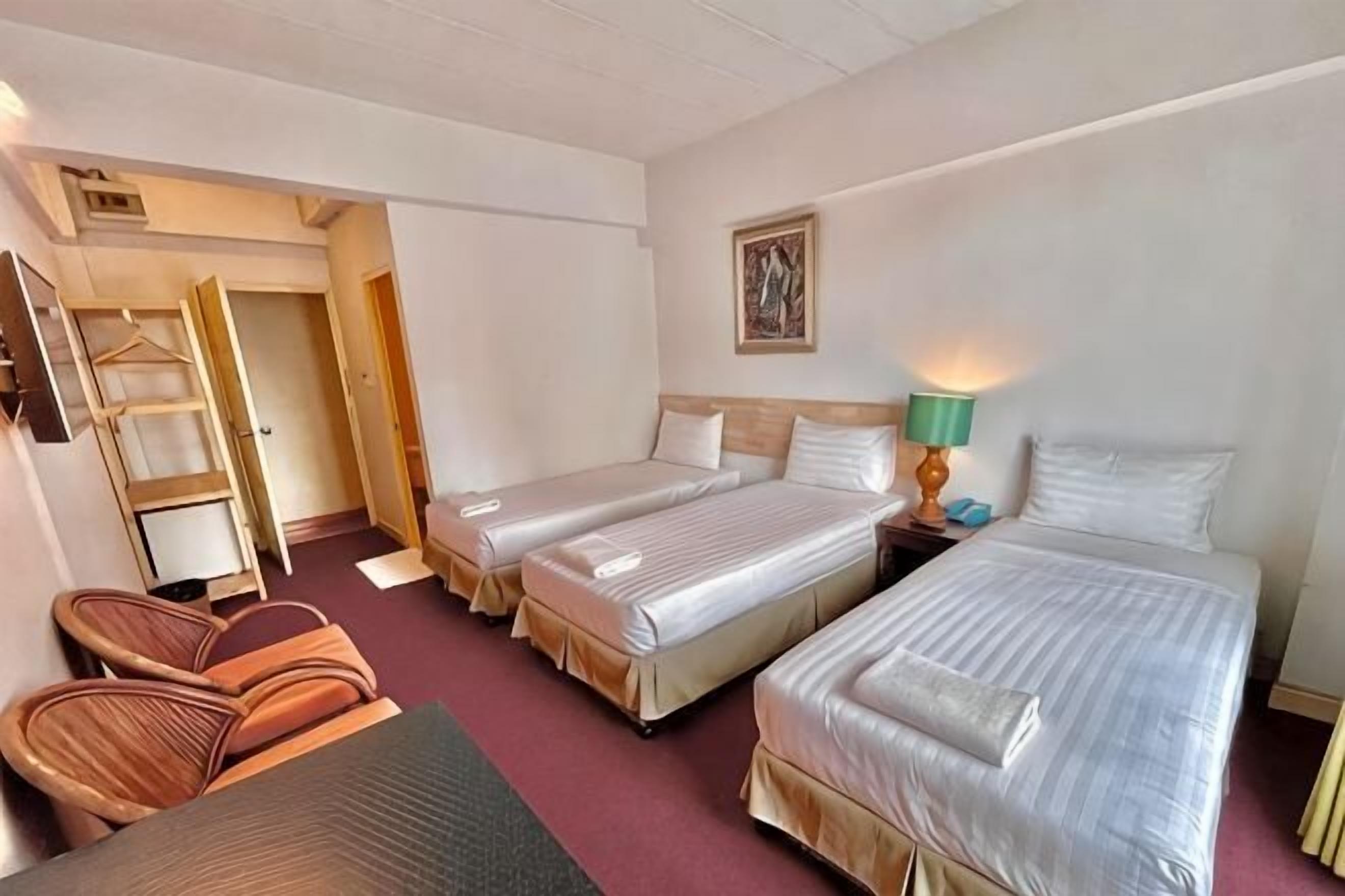 A hotel room with two beds, a chair, a desk, and a wardrobe.