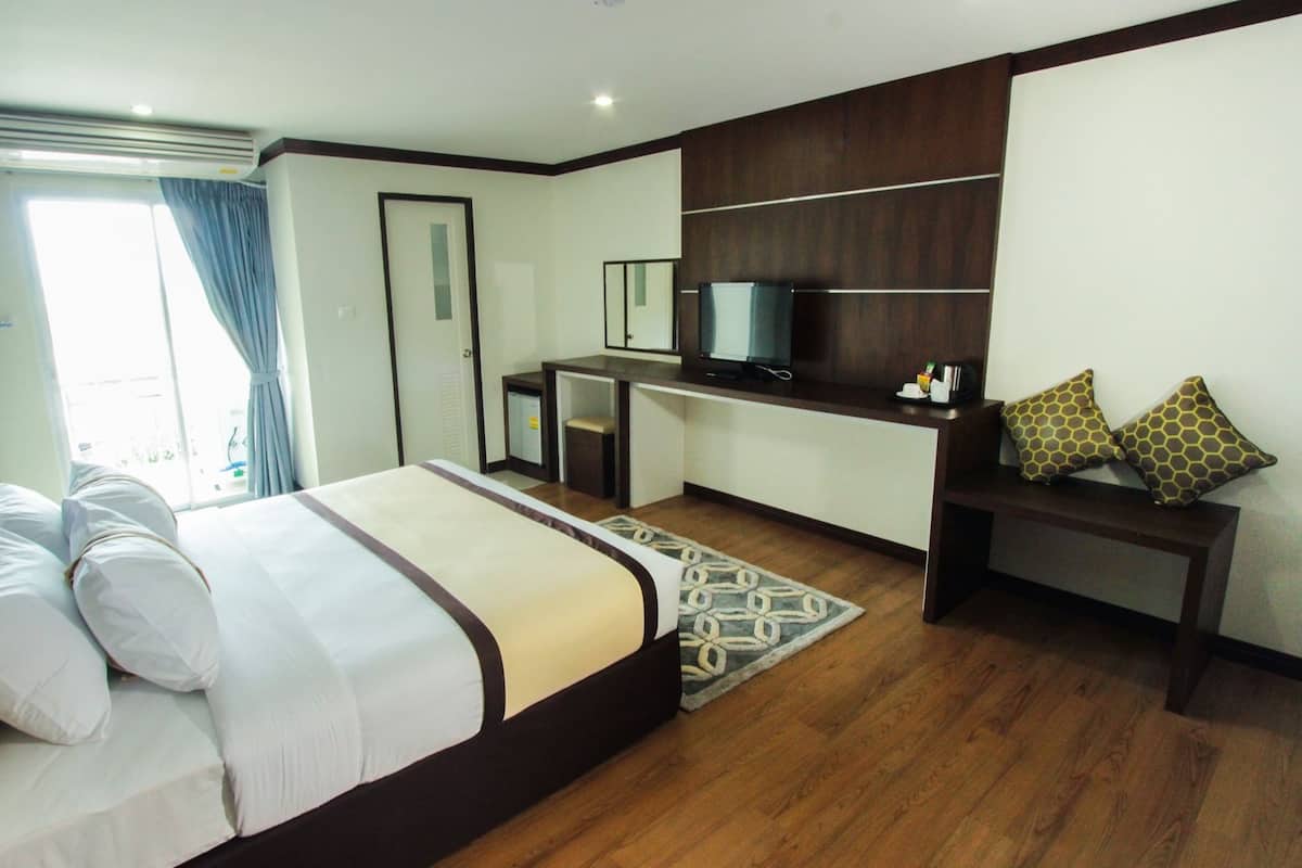 A hotel room with a bed, a desk, a television, and a seating area with patterned cushions.