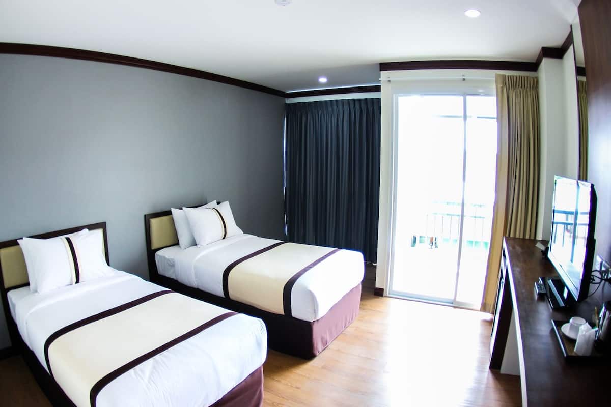 A hotel room with two beds, a TV, and a balcony with curtains.