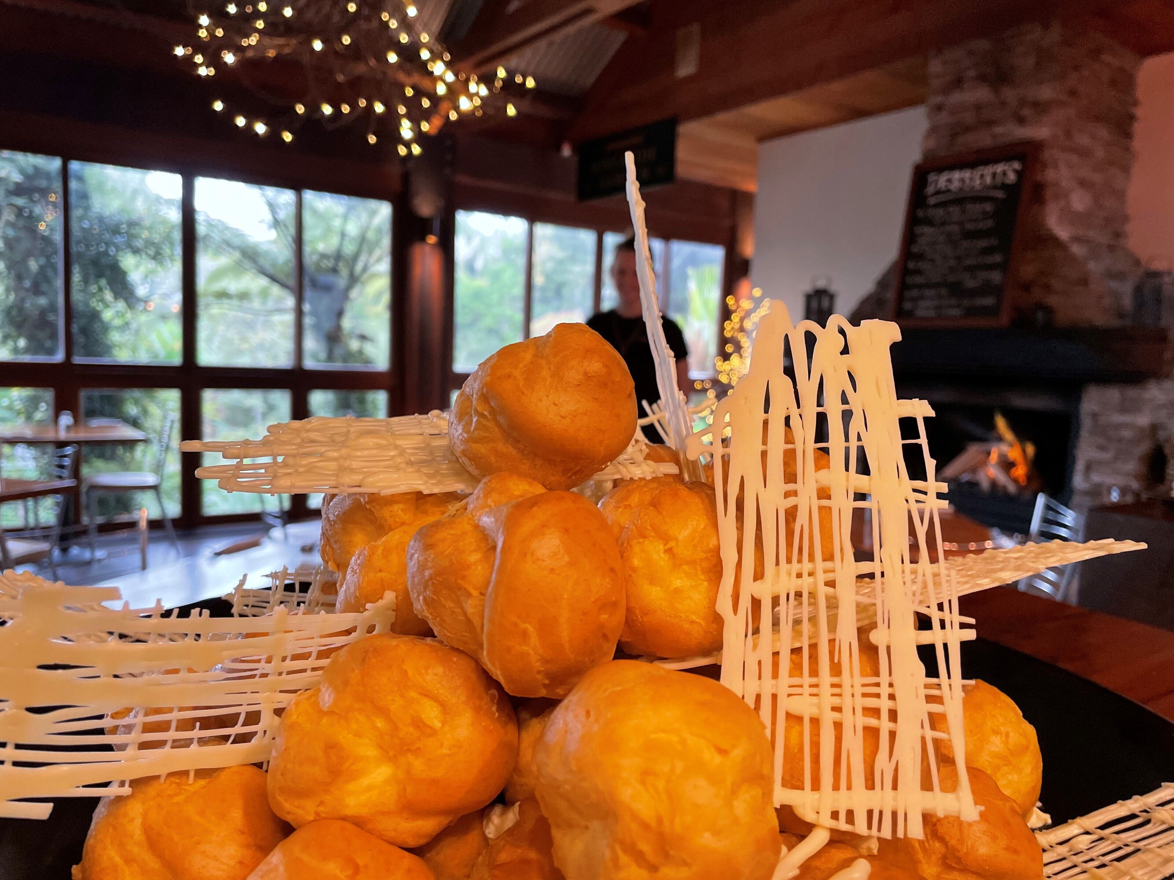 A stack of golden-brown pastries in a basket, with a rustic interior featuring large windows and a stone fireplace.