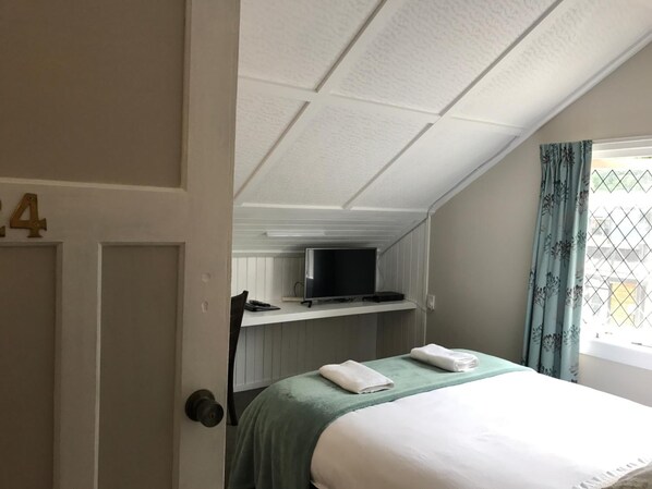 Una habitación de hotel con una cama, un televisor en un estante, una ventana con cortinas y una puerta con un número.