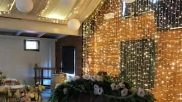 Zona de recepción con un cartel de bienvenida, mesas dispuestas para una boda y luces colgantes en la pared.