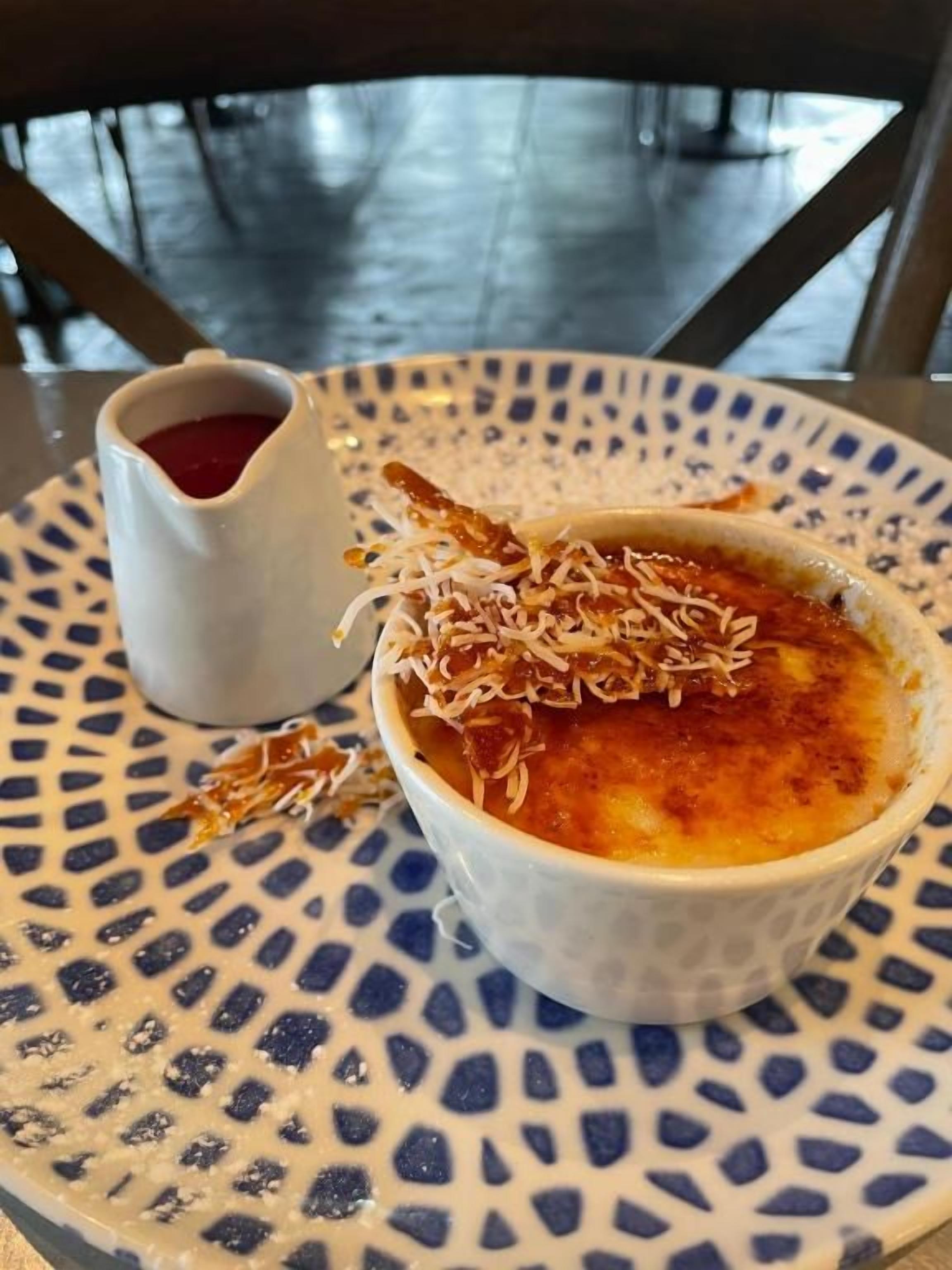 Ein Dessert in einer Schüssel auf einem teller mit Muster, daneben eine kleine Soße.