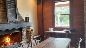 Een rustiek interieur met een stenen openhaard, een houten tafel en stoelen.