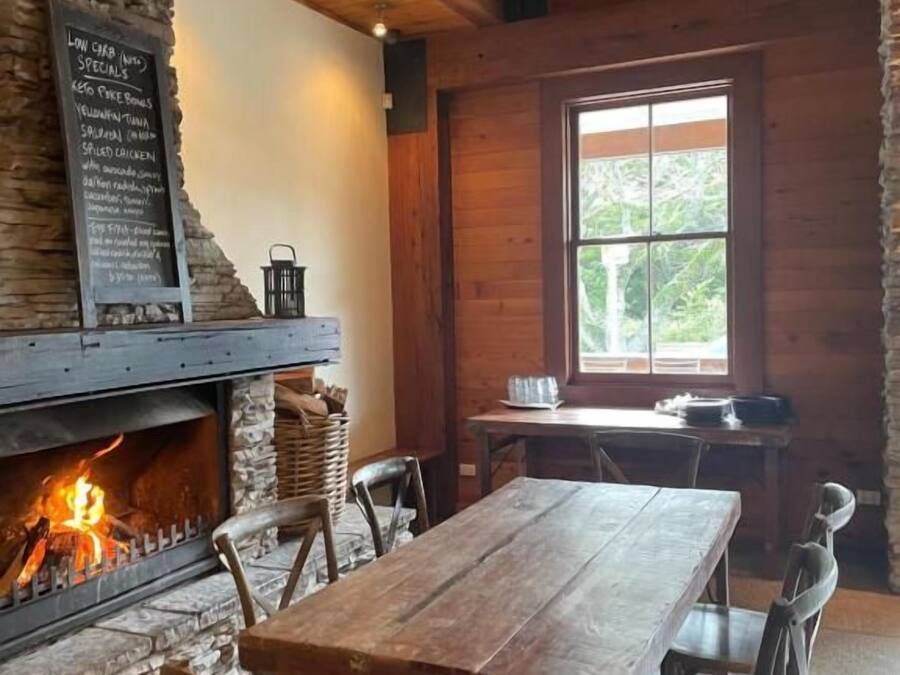 Een rustiek interieur met een stenen openhaard, een houten tafel en stoelen.