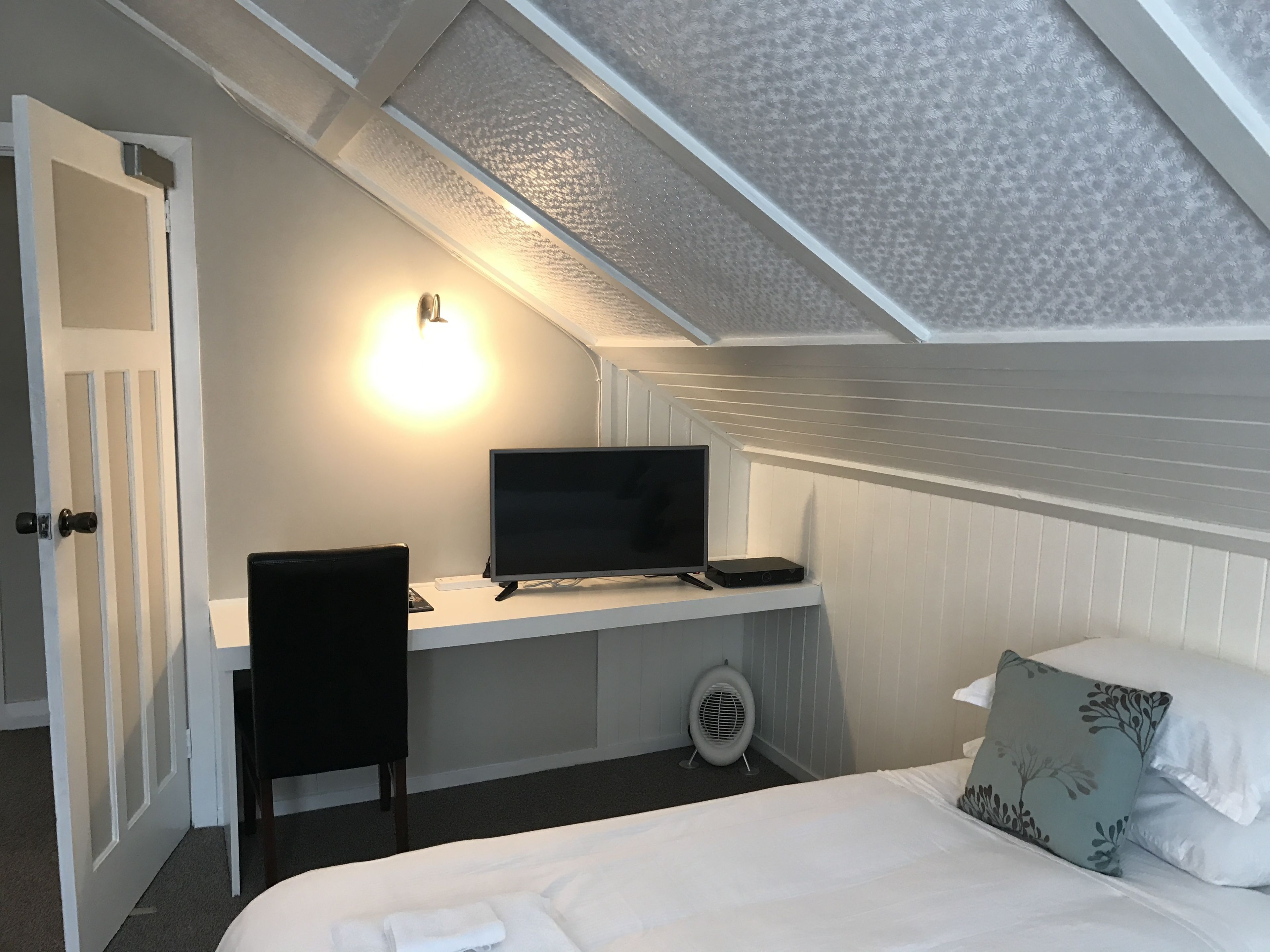 Un dormitorio con cama, escritorio con computadora, silla y mesita de noche.