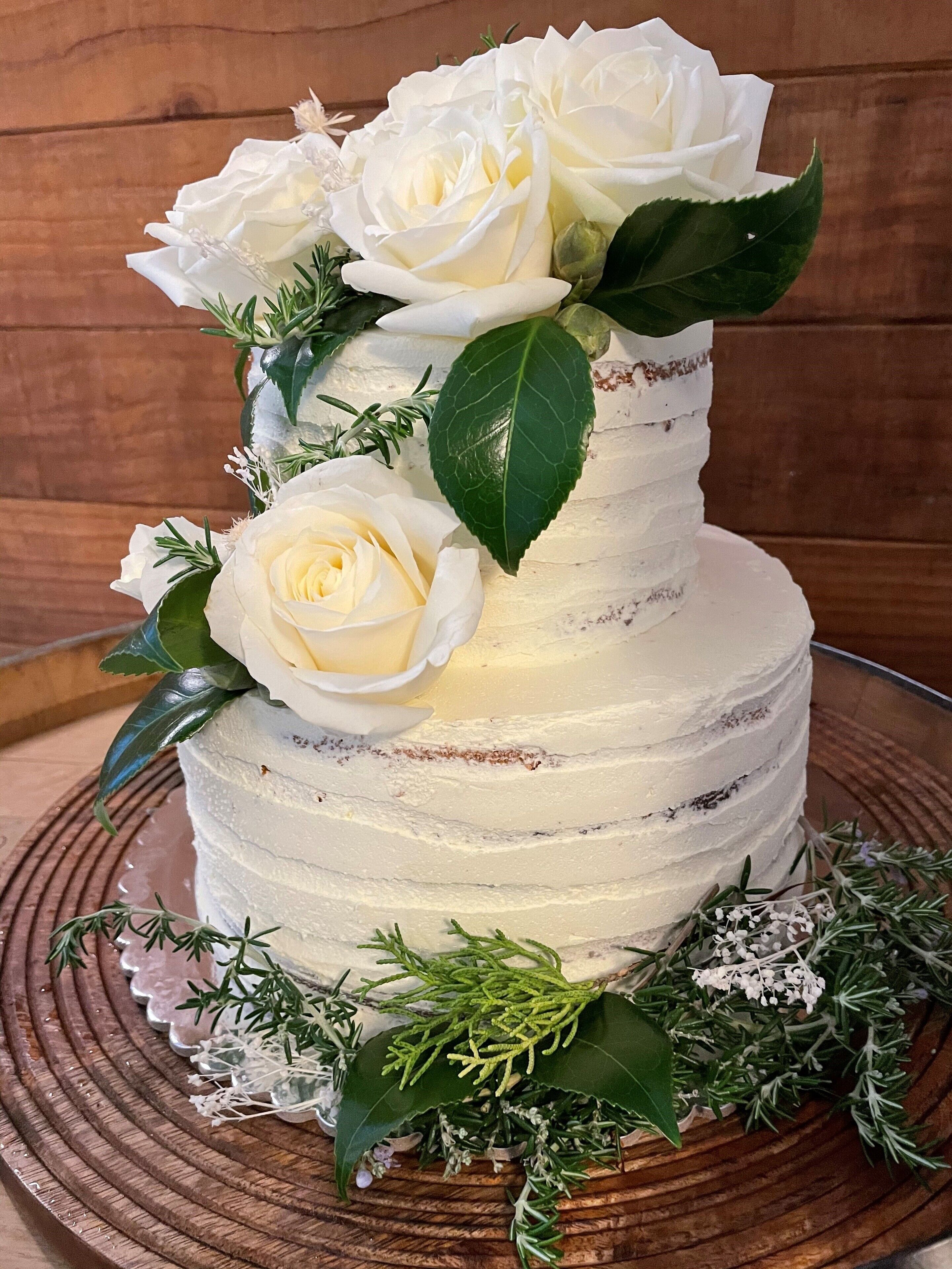 A multi-tiered cake with white frosting and decorated with white roses and green leaves.