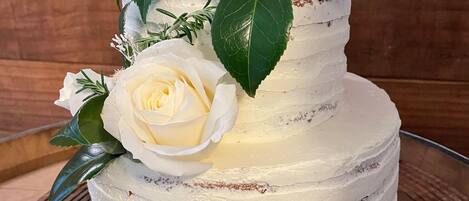 A multi-tiered cake with white frosting and decorated with white roses and green leaves.