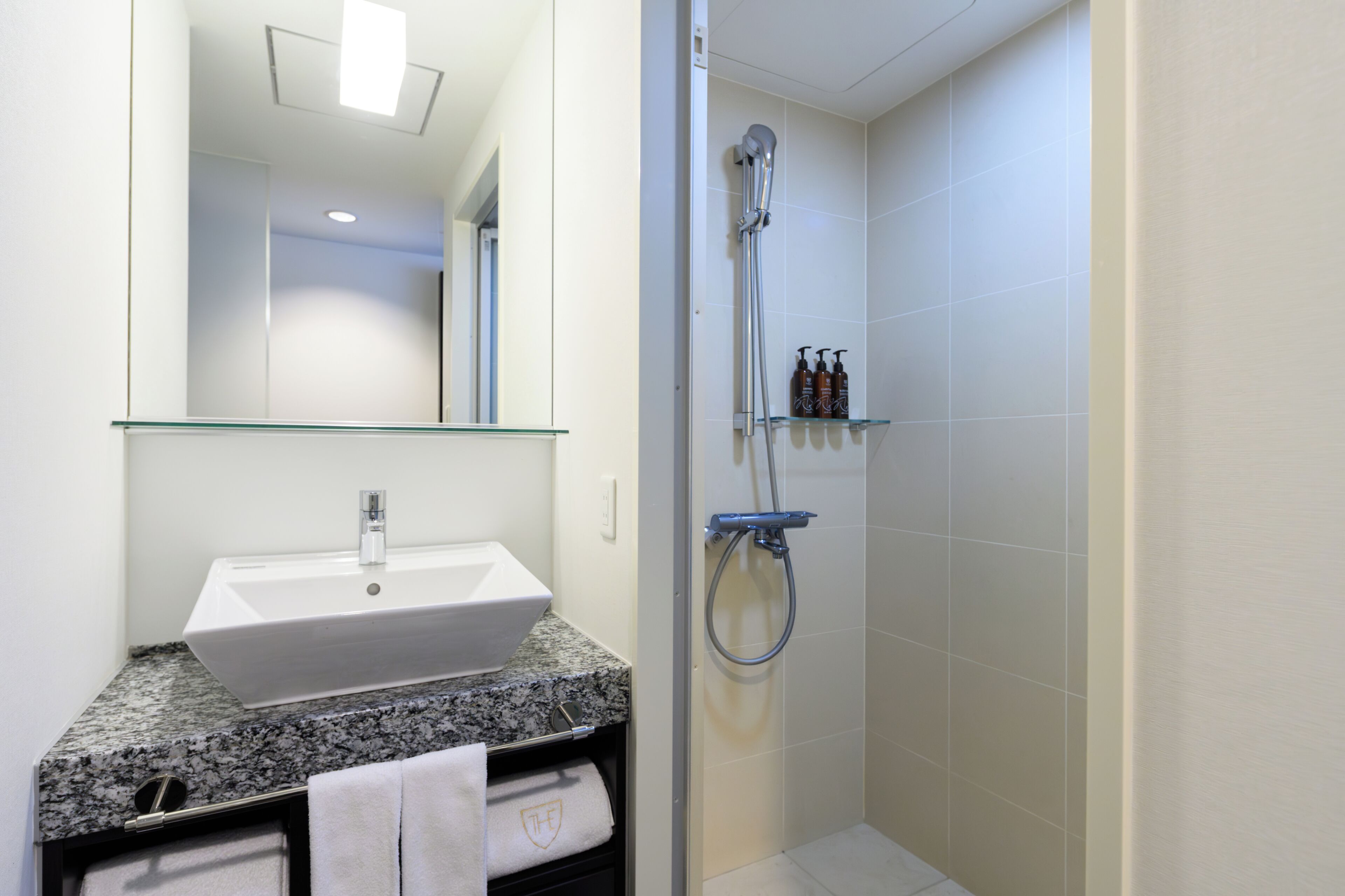 Un bagno con un lavandino bianco, uno scaffale in vetro con articoli da toilette e una doccia.