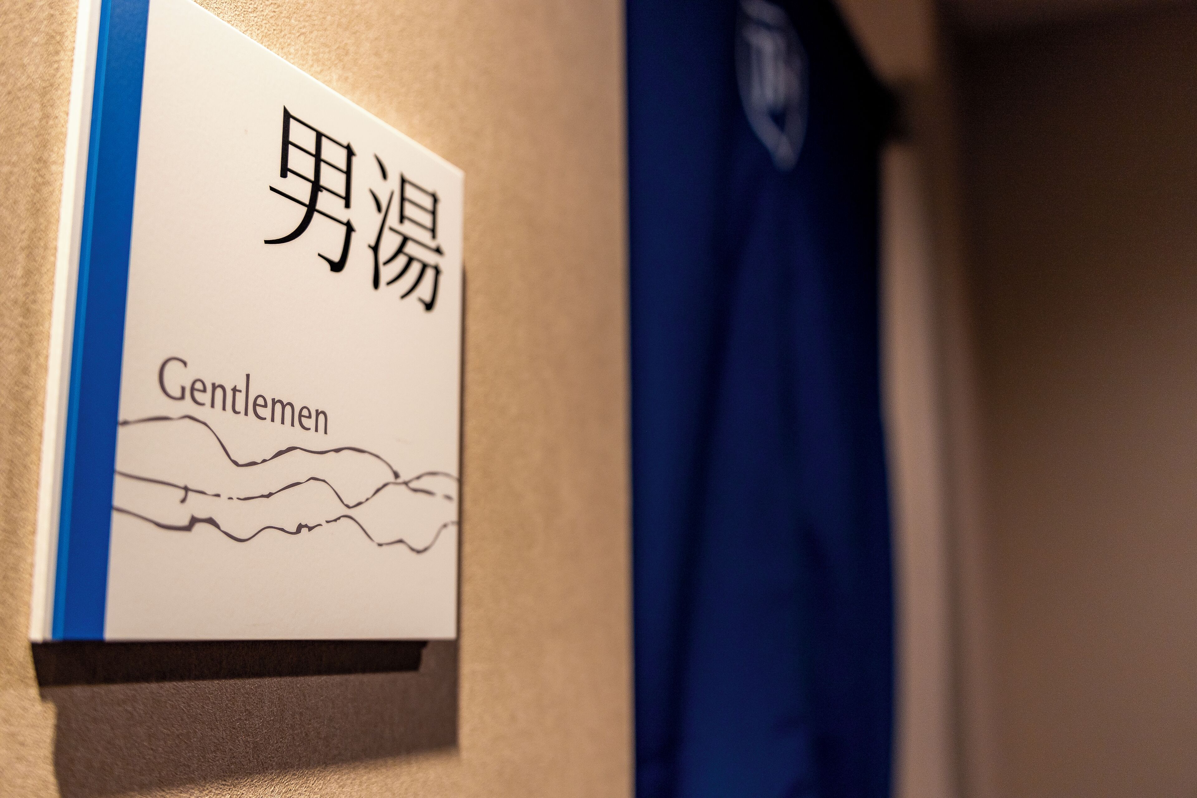 Ein Schild mit japanischen Schriftzeichen und dem englischen Wort 'Gentlemen', das eine Herrentoilette kennzeichnet.