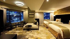 A modern hotel room with a large window, a sofa, a small table, two beds, and a television.