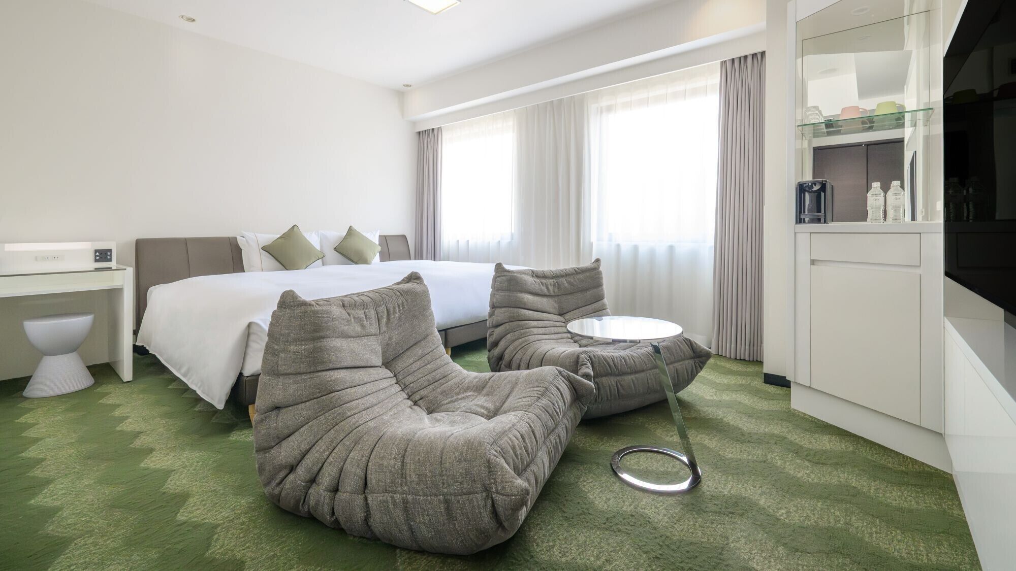 A hotel room with a bed, a desk, a chair, a round table, and a TV.