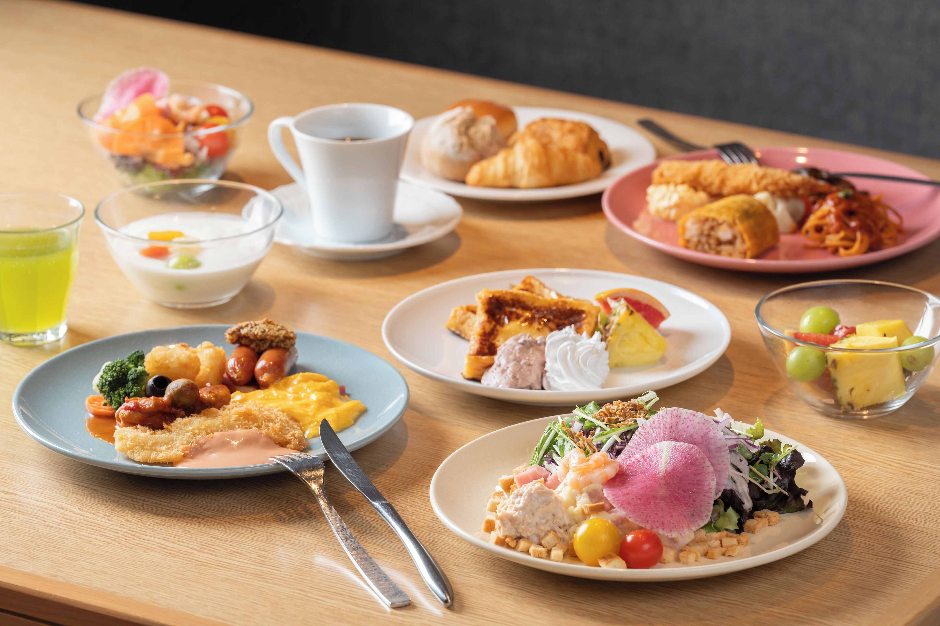 A table with various breakfast dishes including croissants, a salad, and a plate with a fried item.