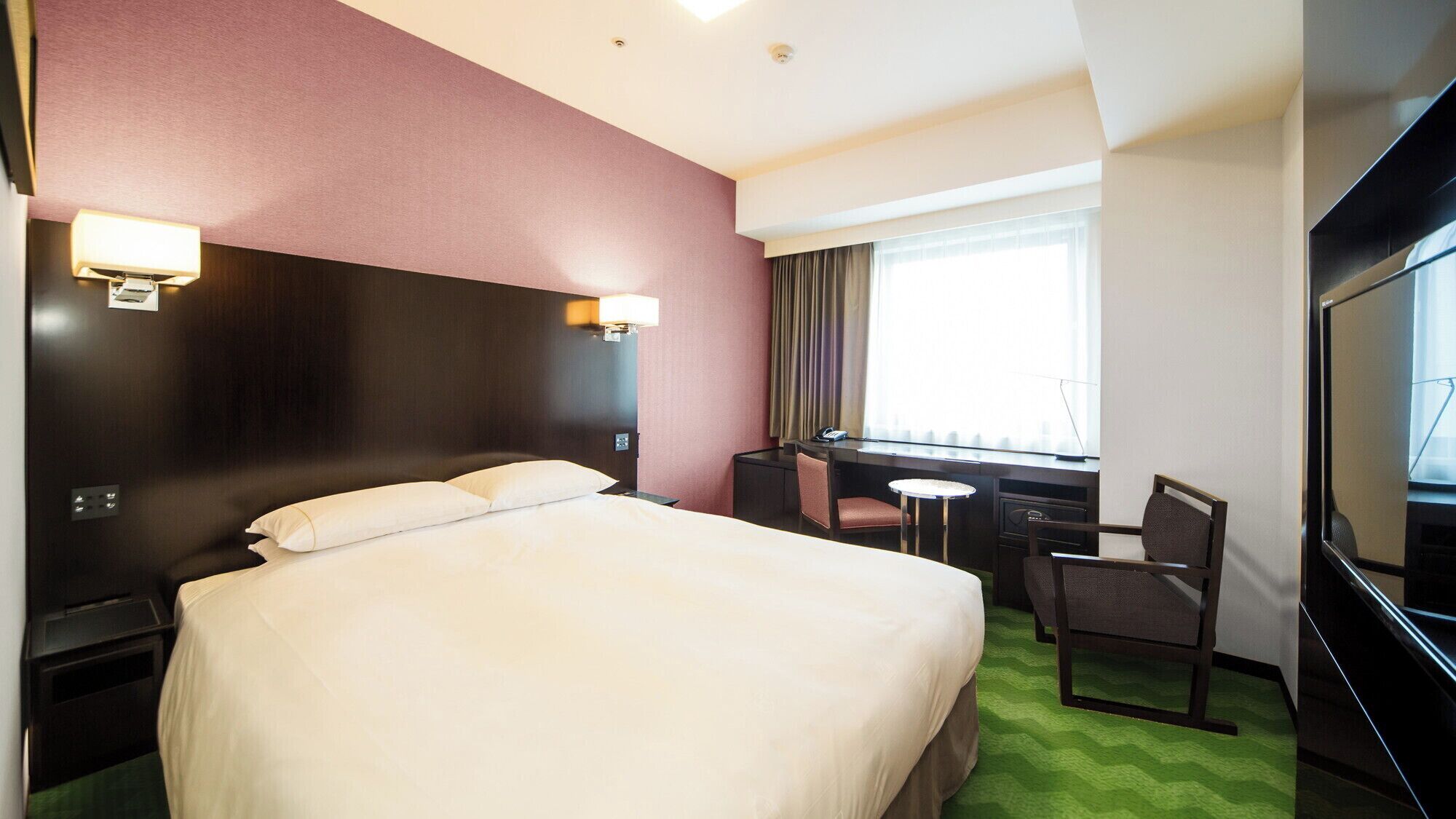 A hotel room with a bed, desk, chair, and TV.