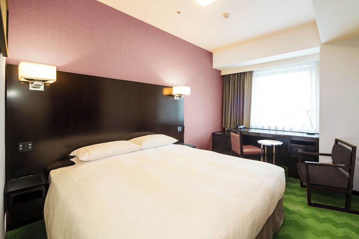 A hotel room with a bed, desk, chair, and TV.