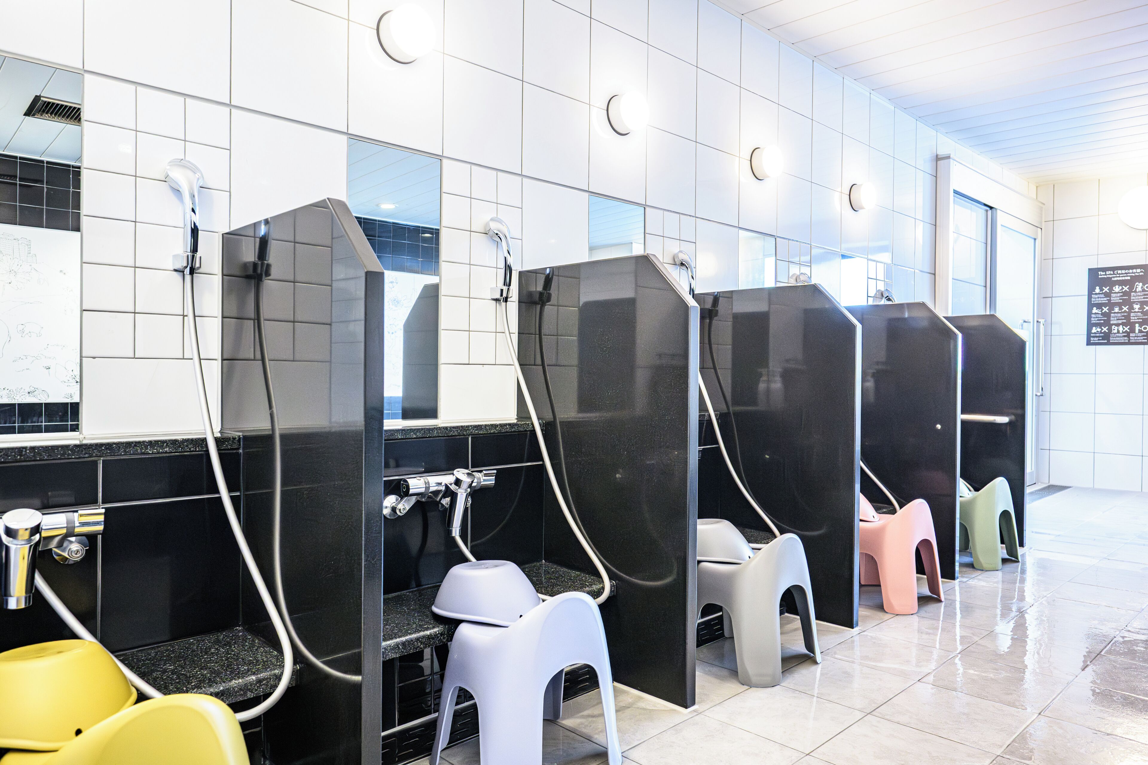A public restroom with multiple stalls, each with a privacy partition and a sink.