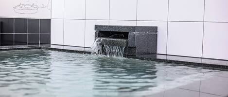 Una piscina con cascada, paredes enlosadas y un barco dibujado en la pared.
