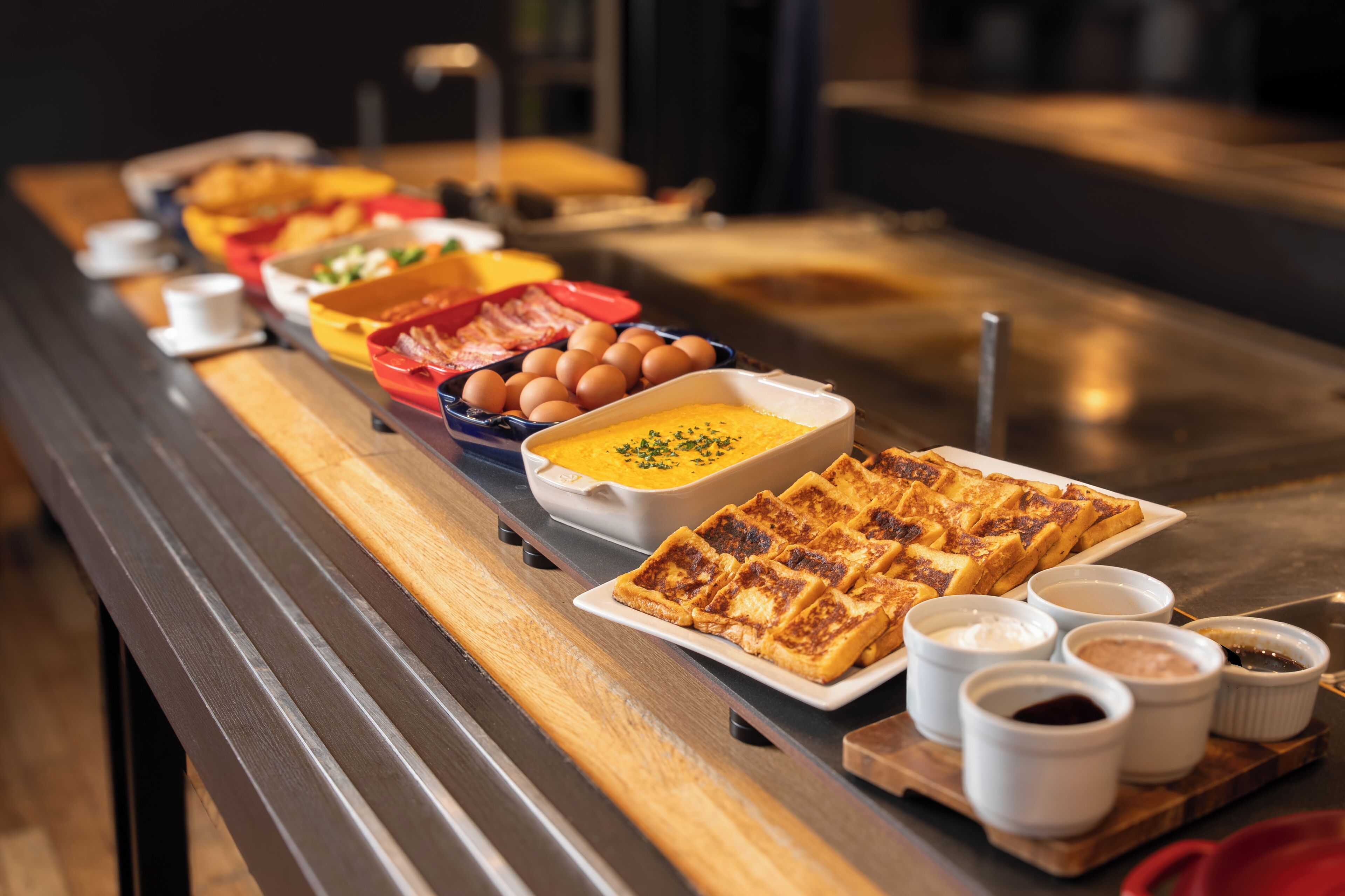 Una mesa de buffet con diversos platos, entre ellos huevos, sopa y gofres.