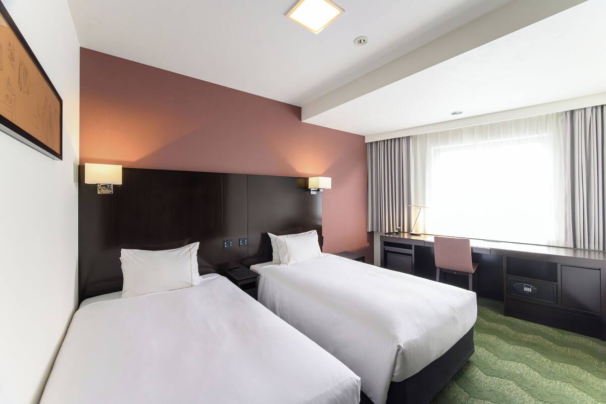 A hotel room with two beds, a desk, and a chair.