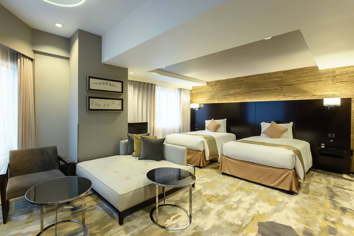 A hotel room with two beds, a sofa, a chair, and a small table.