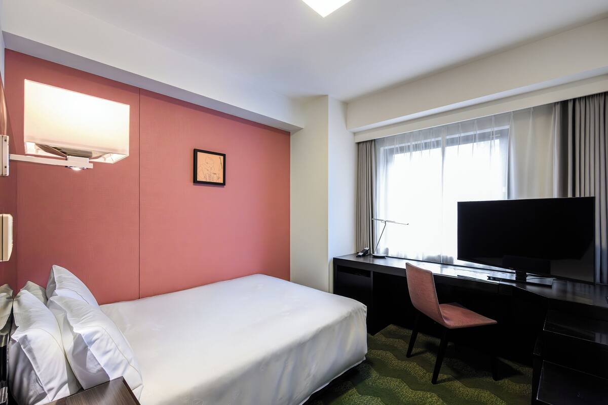 A hotel room with a bed, desk, chair, TV, and a picture on the wall.