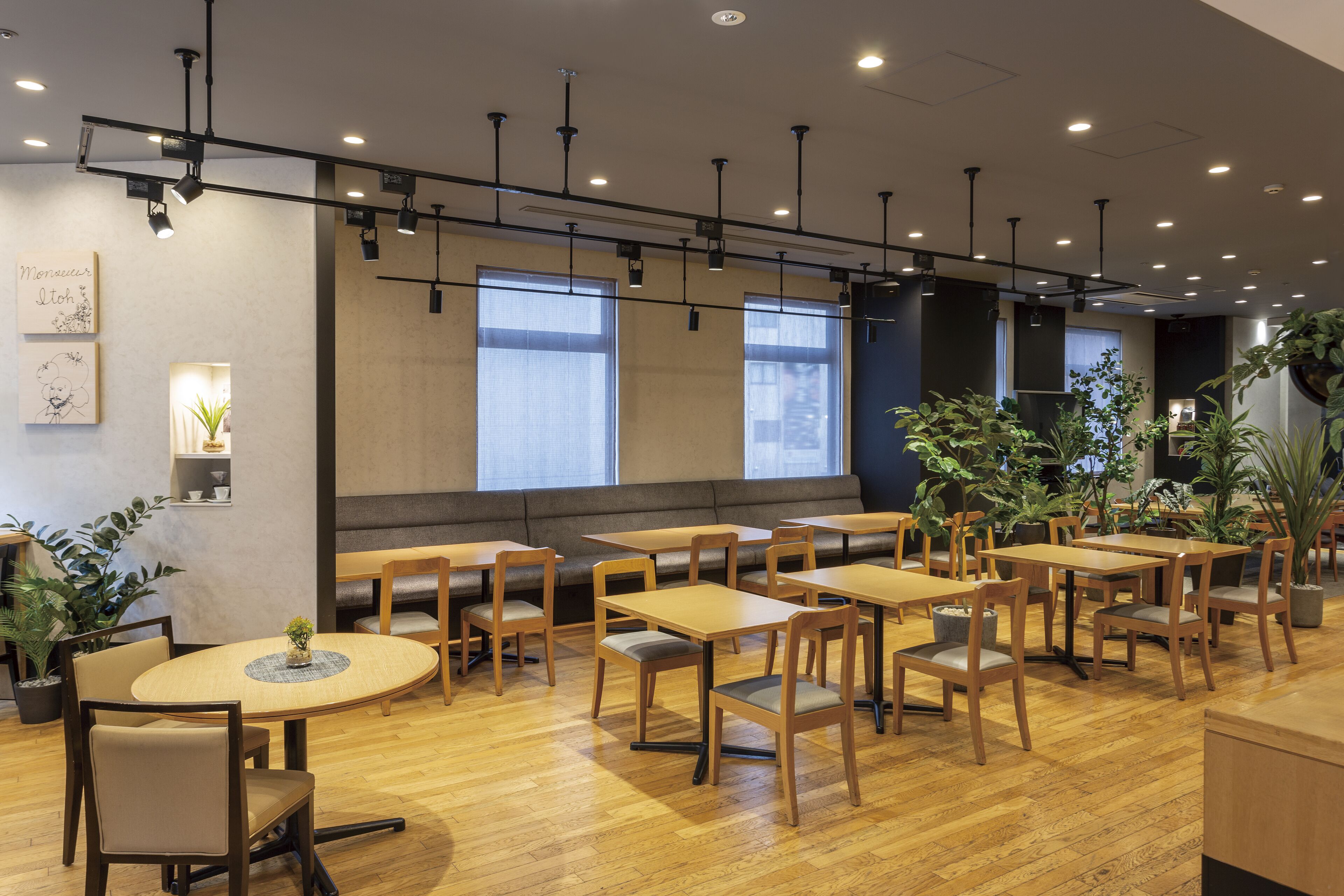 Un restaurant avec des tables et des chaises en bois, de grandes fenêtres et des luminaires au plafond.