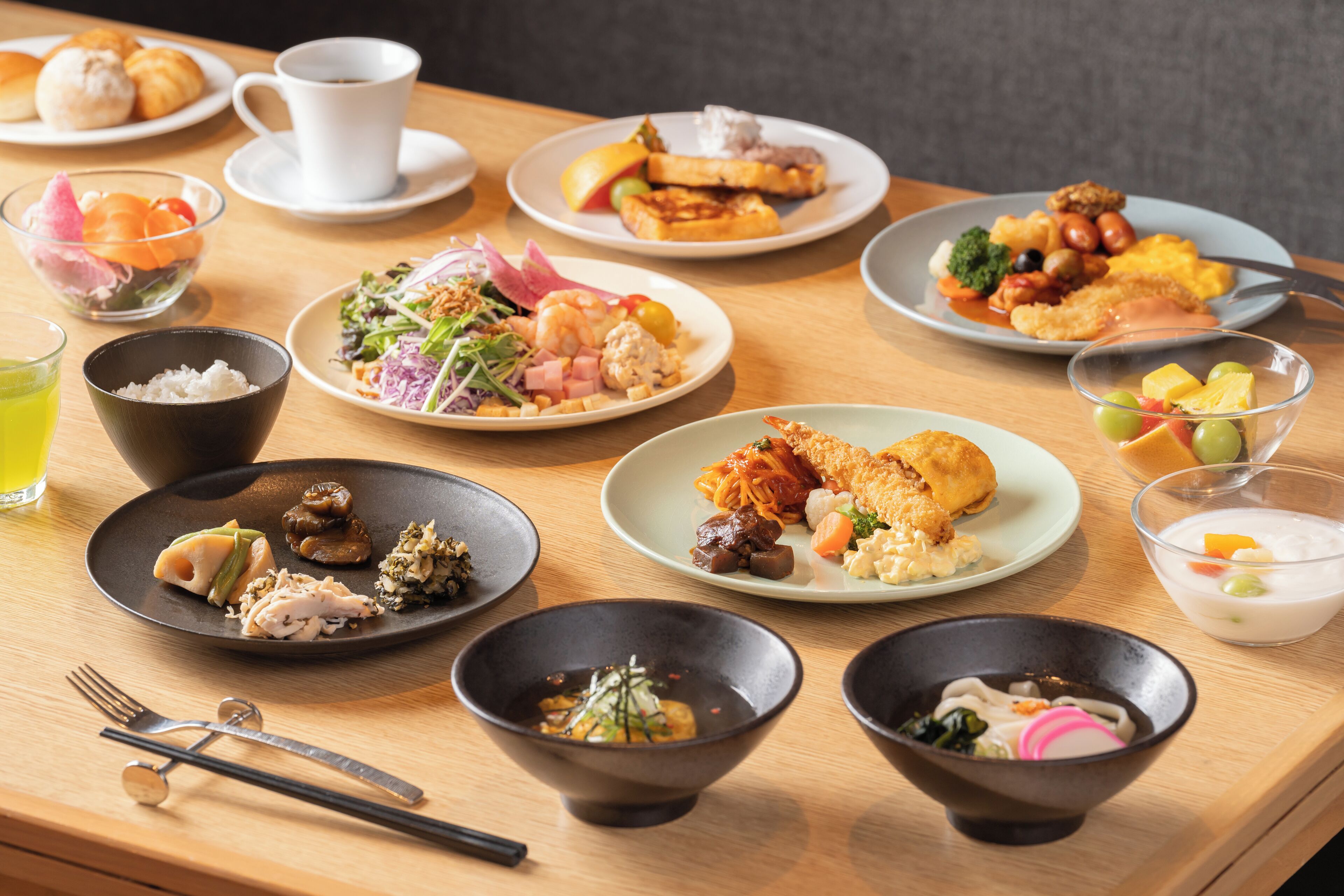 A variety of dishes on a wooden table, including plates with different foods and bowls of soup.