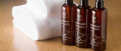 Three brown bottles with black pumps, labeled "THE" and "BODY WASH," alongside a white towel on a wooden surface.