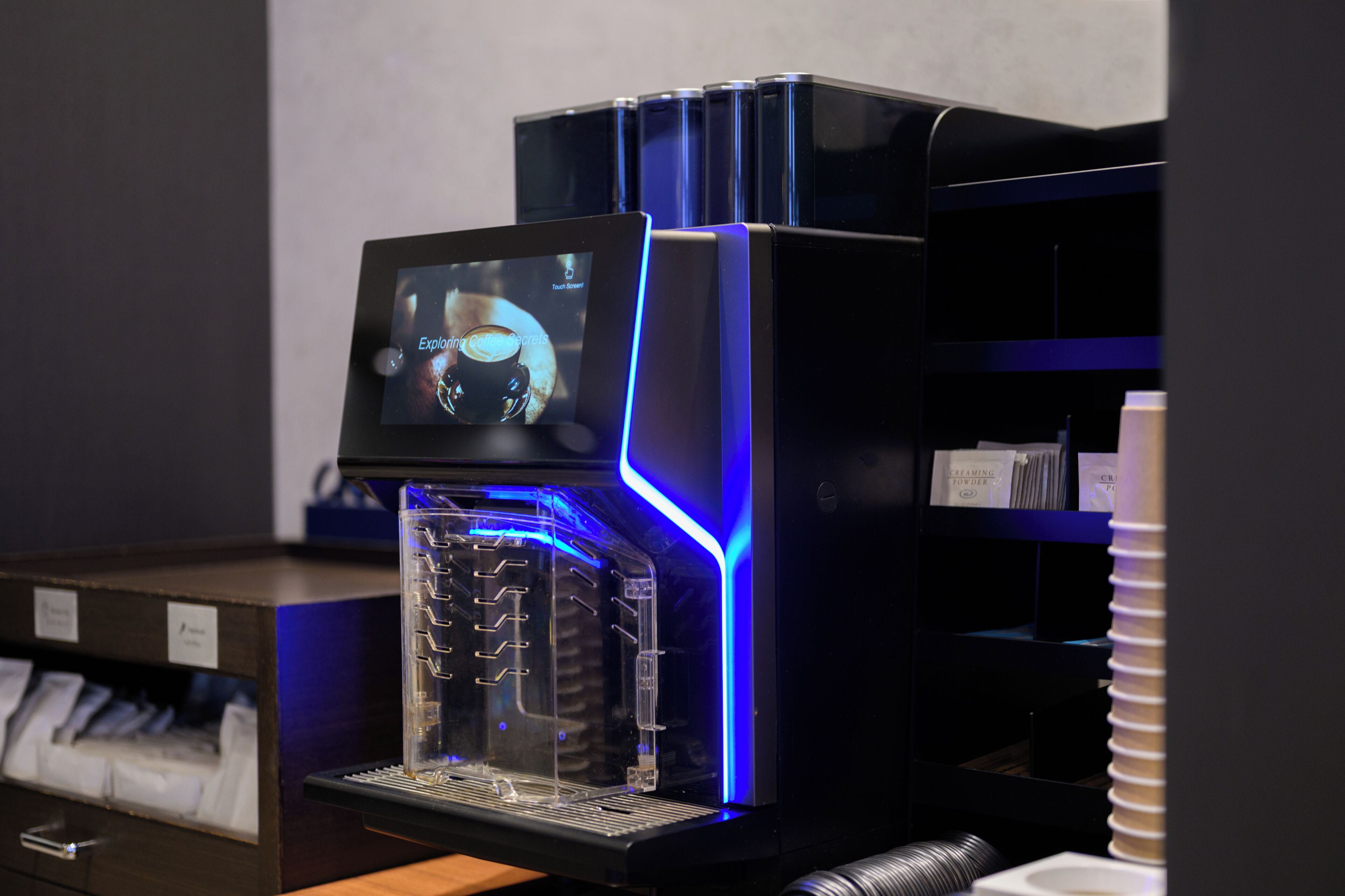 A coffee machine with a digital display, a clear water tank, and a blue-lit exterior.