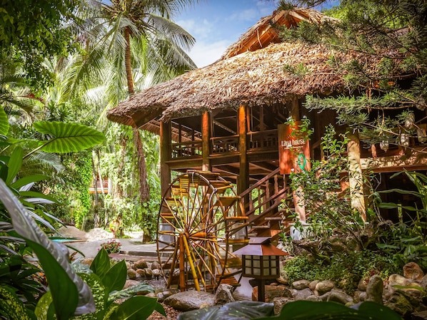 A traditional thatched-roof structure with a wooden staircase leading to a platform, surrounded by lush tropical vegetation. - Furama Villas Danang (Da Nang)