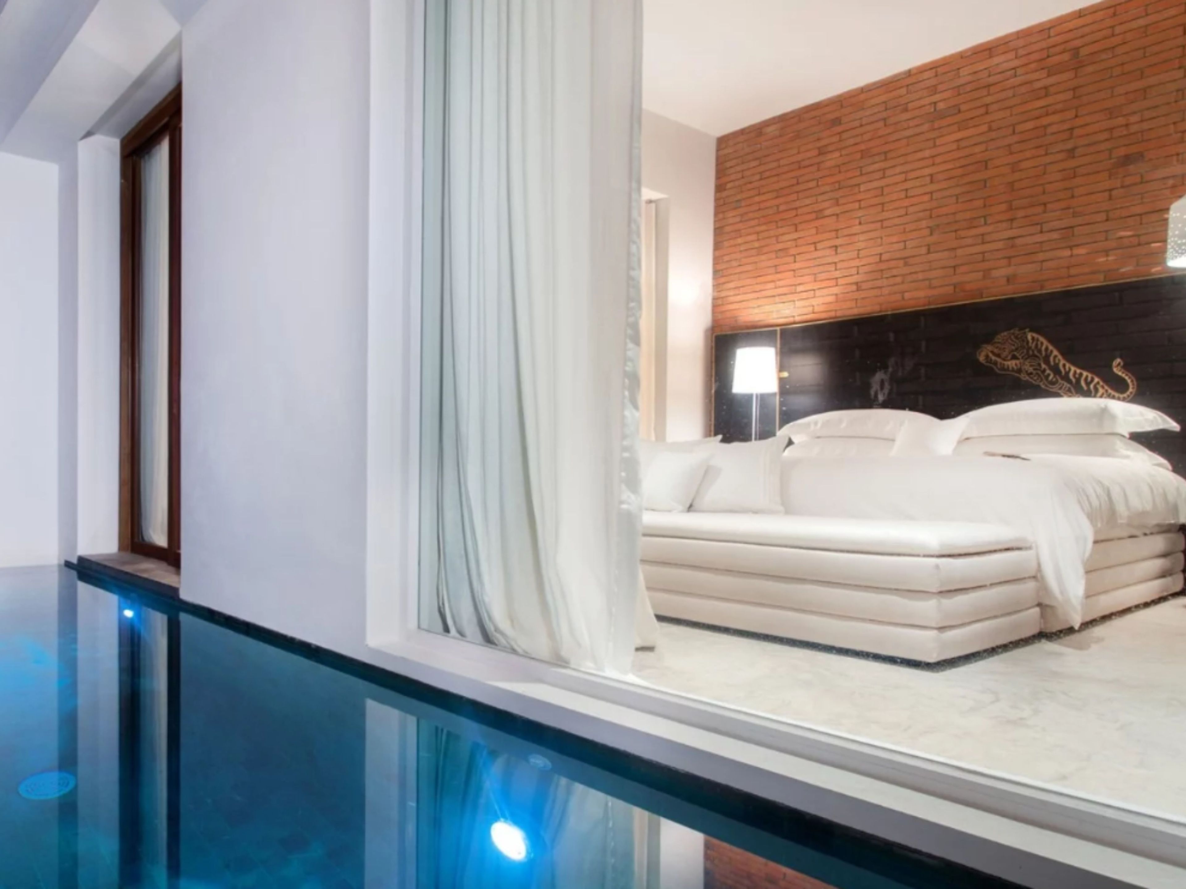 A modern hotel room with a glass balcony, a brick accent wall, and a white sofa.