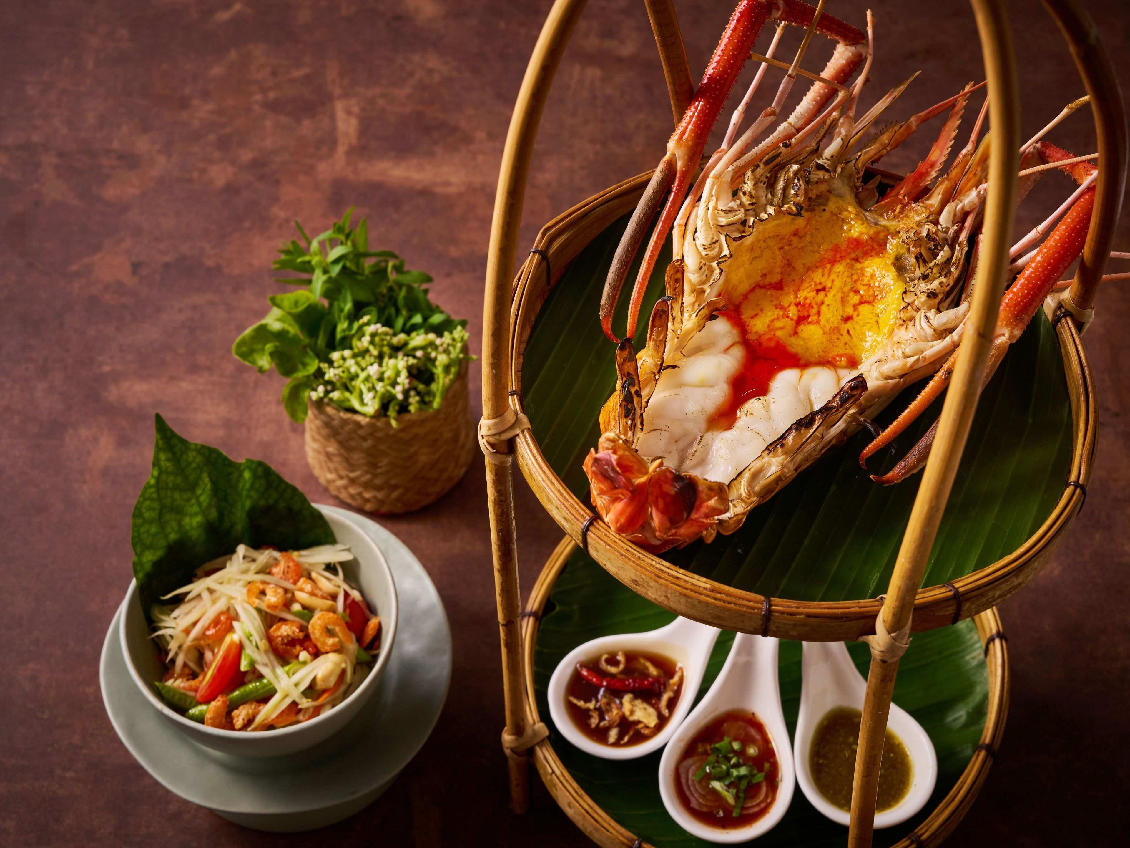 A dining setup with a crab on a bamboo stand, a bowl of salad, and two small bowls of sauce.