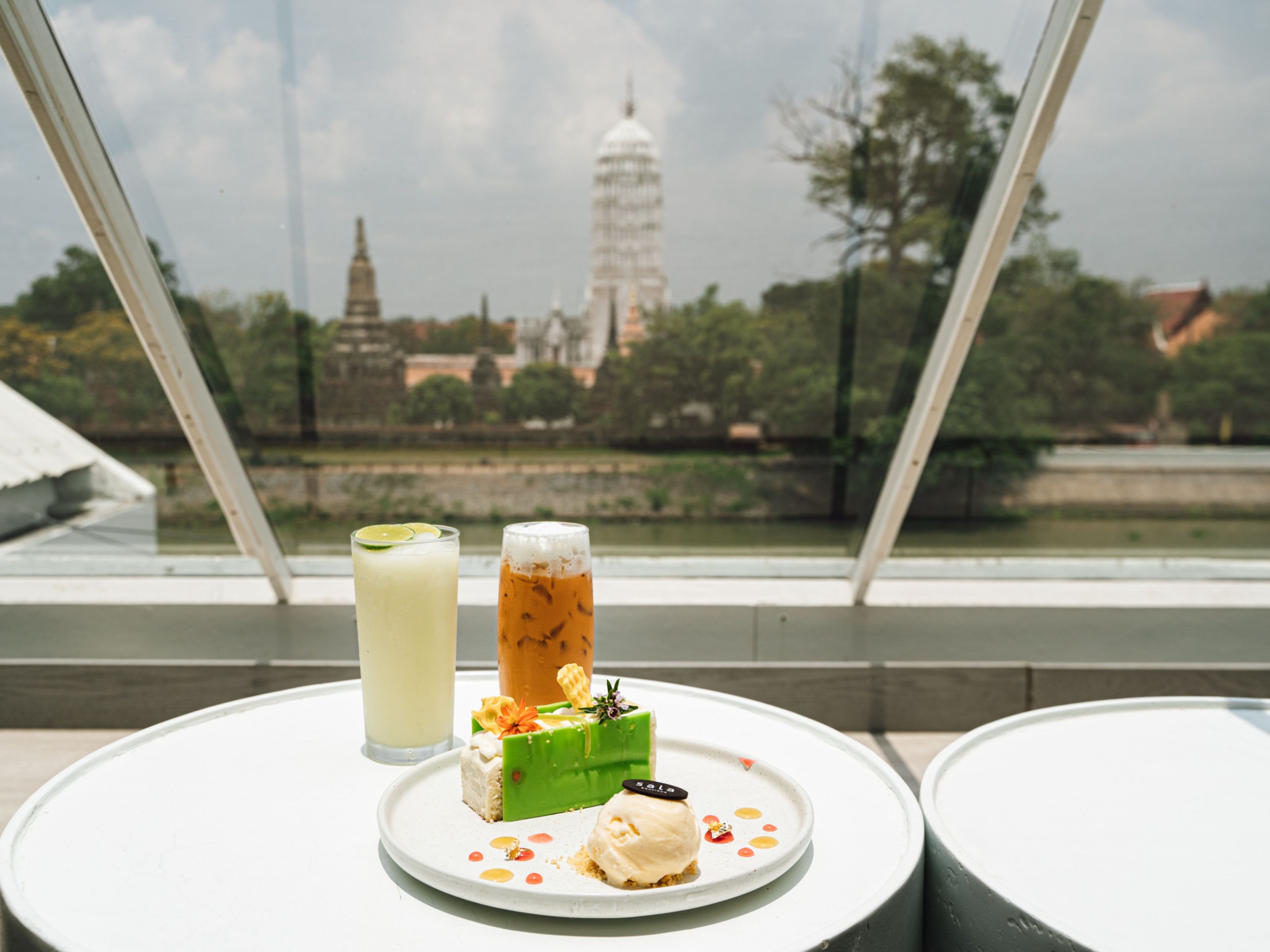 A table with a dessert and drinks, overlooking a cityscape with a prominent tower.