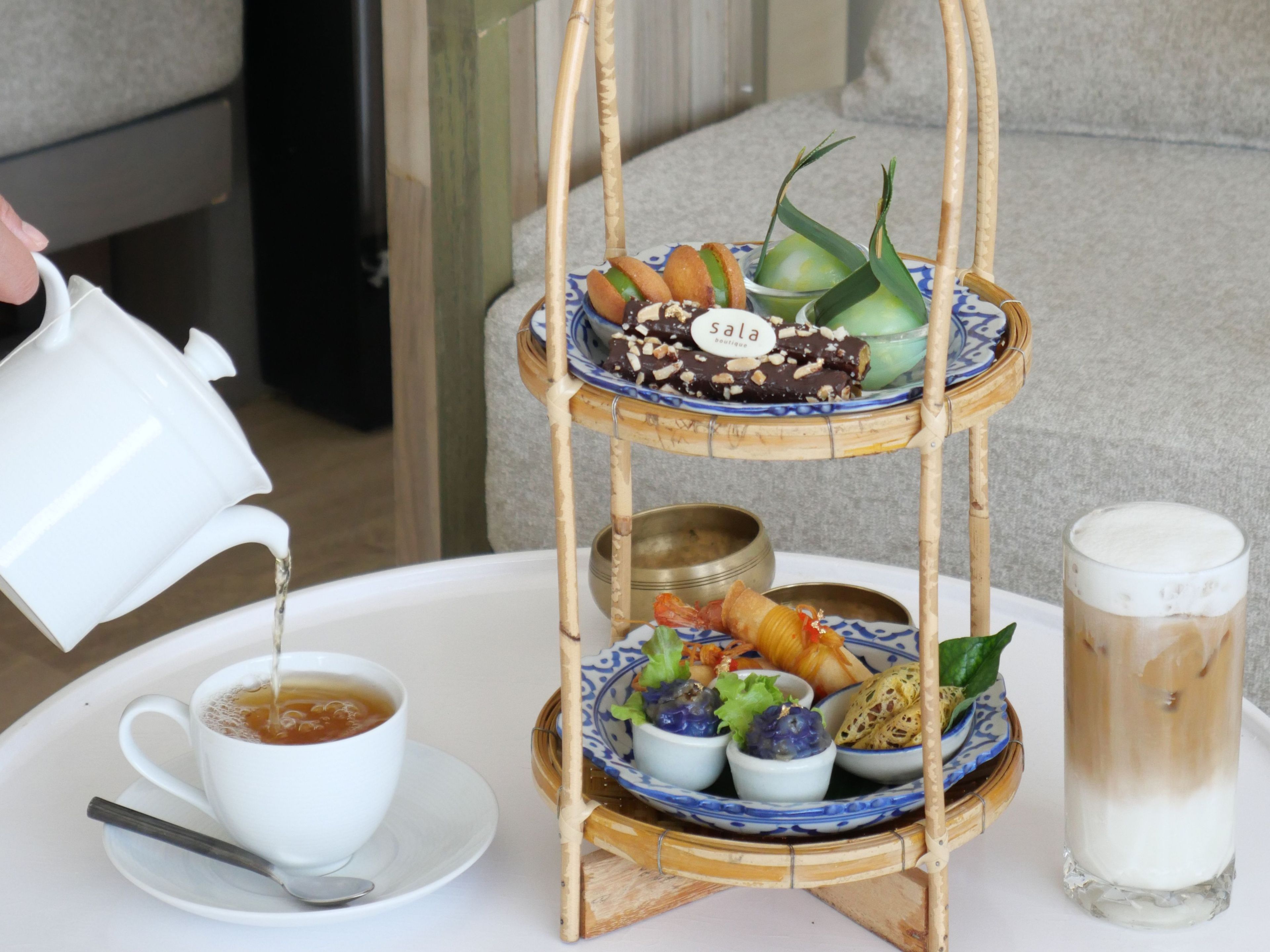 A three-tiered tray with various food items and a cup of tea on a table.