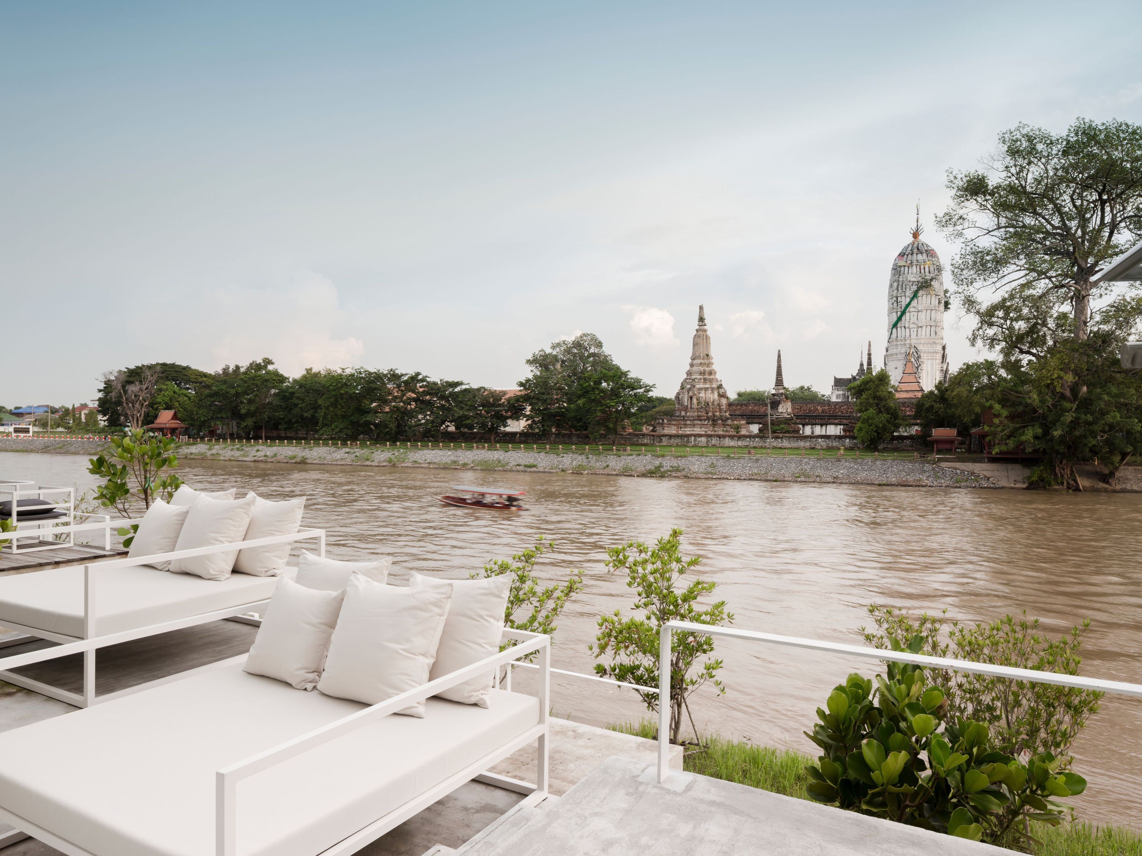 Vista al río con un comedor con asientos blancos al aire libre y una vista de un templo con una aguja imponente.