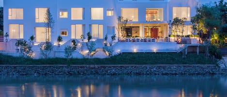 A modern multi-story building with large windows and a flat roof, situated next to a body of water.
