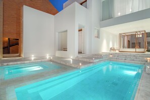 Un área de piscina moderna con agua cristalina, escalones de acceso y una estructura de madera a la derecha.