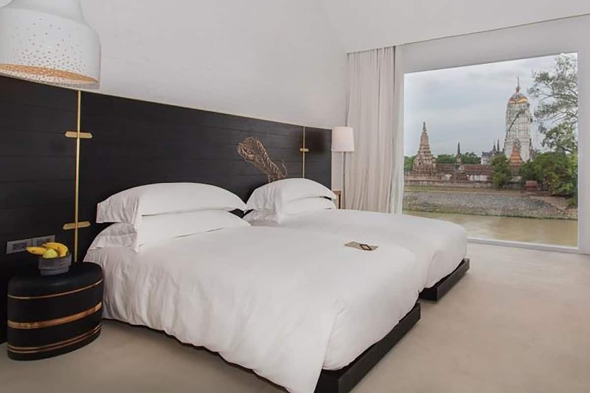 A modern hotel room with two beds, a large window with a view of a temple, and a decorative wall piece.