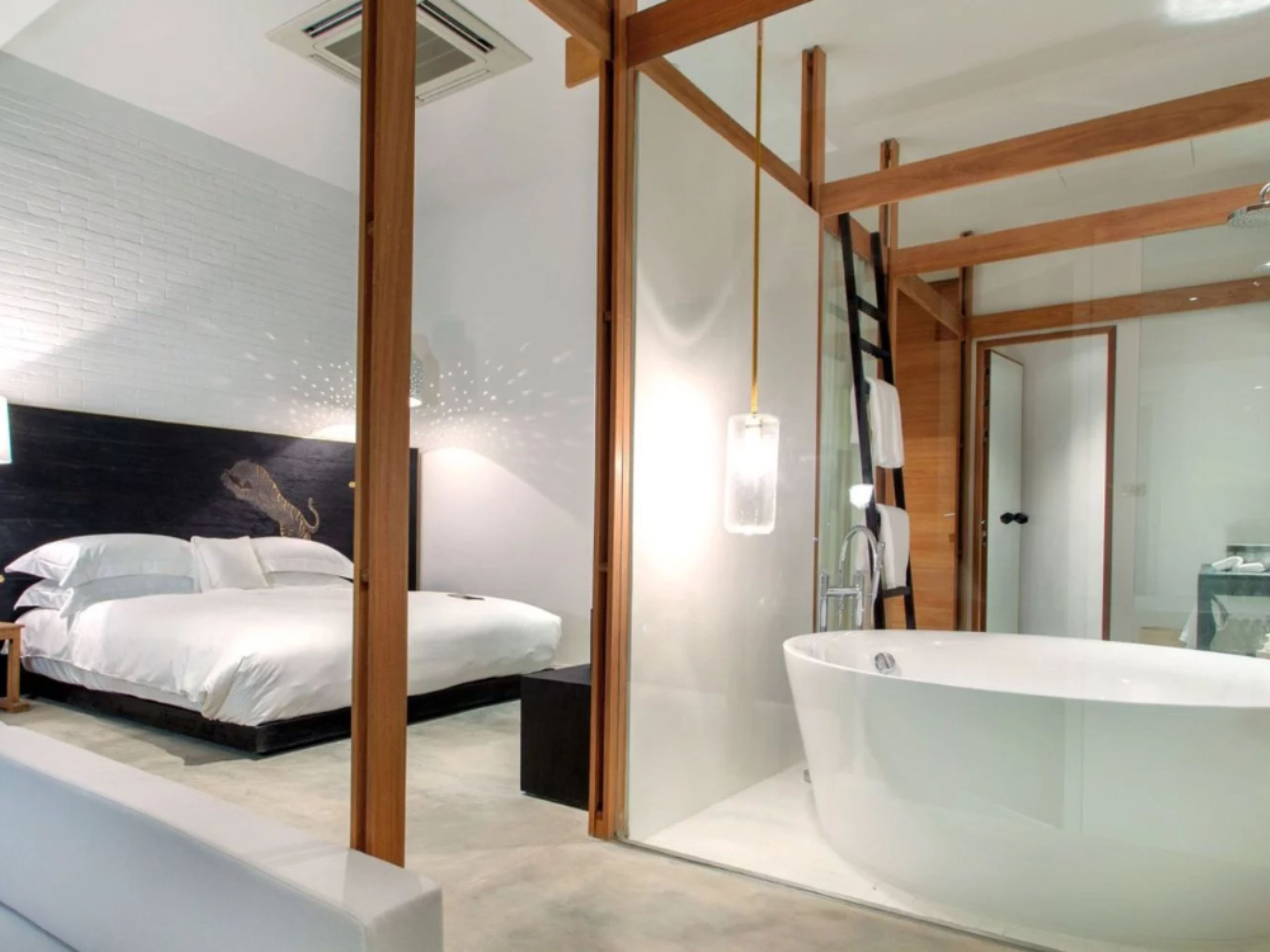 A modern bedroom with a large bed, a built-in bathtub, and a wooden ceiling structure.