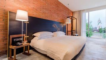 A hotel room with a brick wall, a large bed, two bedside tables, and a view of a temple through the window.