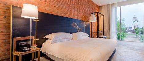 A hotel room with a brick wall, a large bed, two bedside tables, and a view of a temple through the window.
