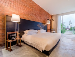 A hotel room with a brick wall, a large bed, two bedside tables, and a view of a temple through the window.
