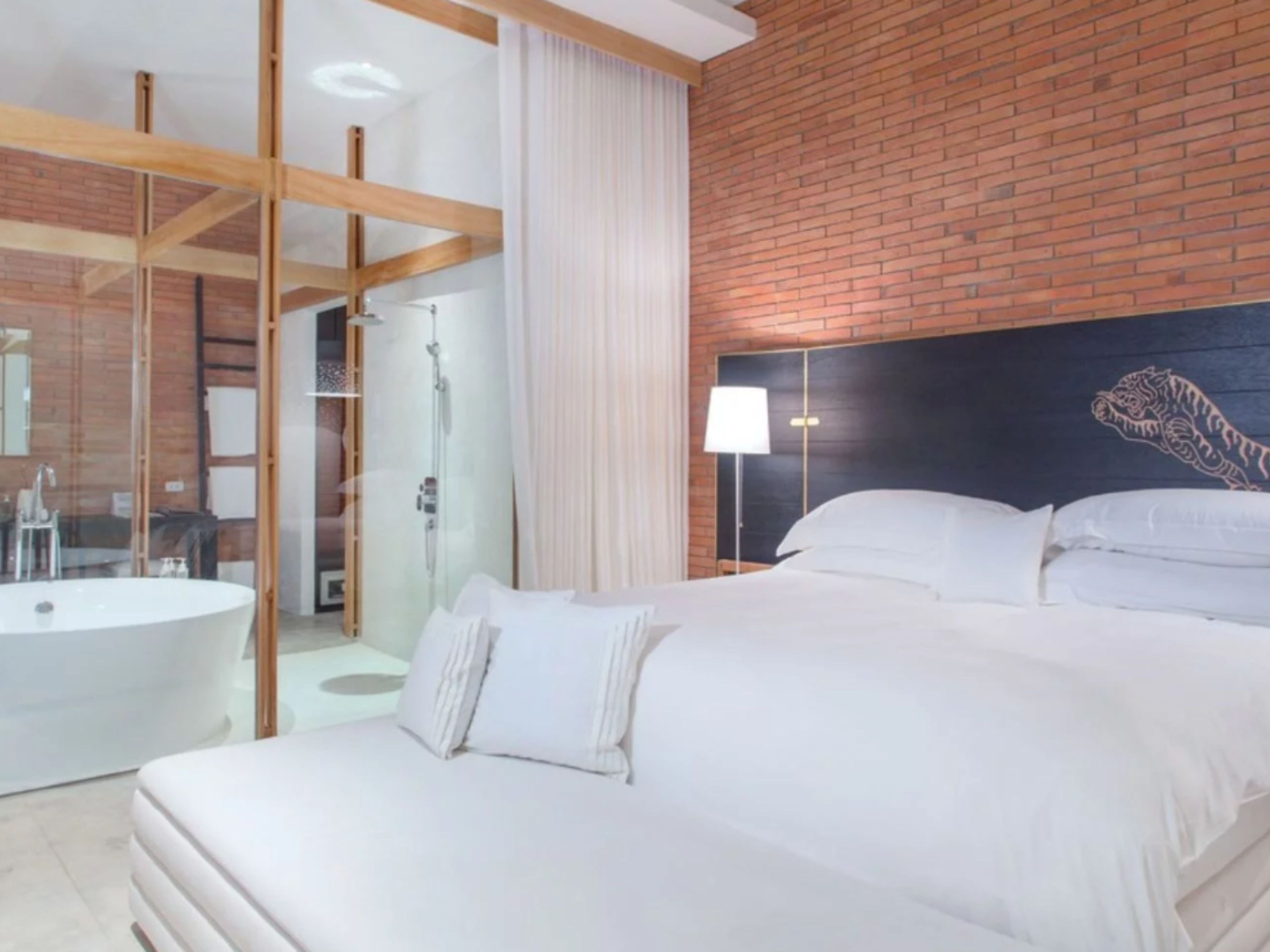 A modern hotel room with a large bed, a bathroom with a bathtub, and a brick wall.