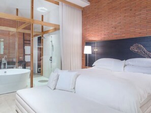 A modern hotel room with a large bed, a bathroom with a bathtub, and a brick wall. - Sala Ayutthaya (Ayutthaya)